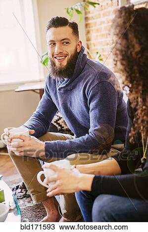 Stock Image - Couple drinking coffee on sofa in living room. Fotosearch