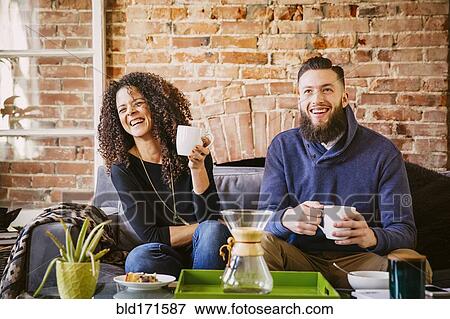 Stock Photo - Couple drinking coffee on sofa in living room. Fotosearch