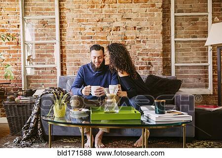 Stock Photo - Couple drinking coffee on sofa in living room. Fotosearch