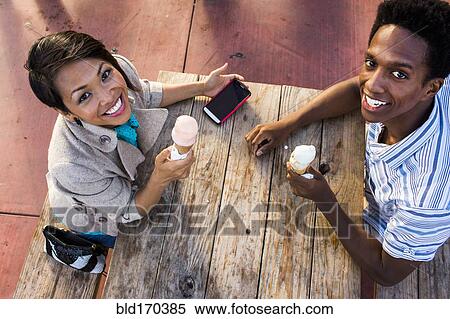 Stock Photography - Couple eating ice cream and using cell phone at picnic table. Fotosearch