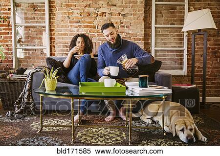 Stock Photography - Couple enjoying breakfast on sofa in living room. Fotosearch