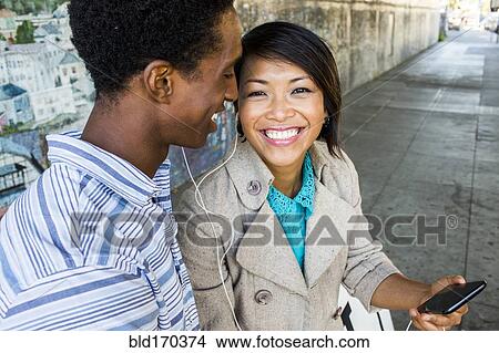 Couple listening to cell phone on city sidewalk View Large Photo Image Picture - Couple listening to cell phone on city sidewalk. Fotosearch