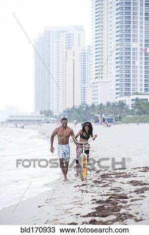 Couple riding bicycle on urban beach View Large Photo Image Stock Image - Couple riding bicycle on urban beach. Fotosearch