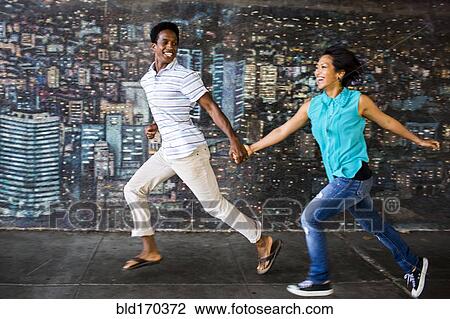 Stock Image - Couple running by mural on city sidewalk. Fotosearch