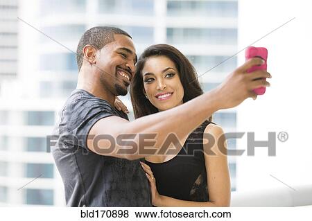 Stock Photo - Couple taking selfie with cell phone on urban balcony. Fotosearch