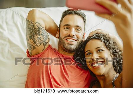 Stock Photo - Couple taking selfie with cell phone on bed. Fotosearch