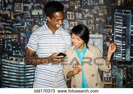 Stock Image - Couple using cell phone by mural. Fotosearch