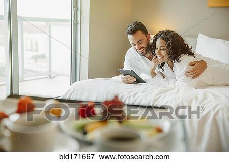 Stock Photo - Couple using digital tablet on hotel bed. Fotosearch