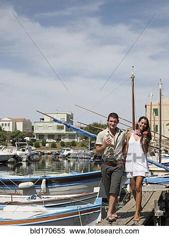 Stock Photography - Couple walking on wooden dock in urban harbor. Fotosearch