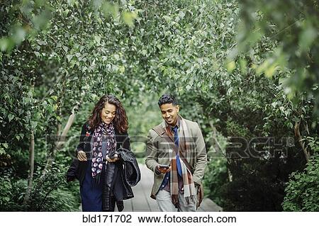 Stock Image - Couple walking on wooden walkway in park. Fotosearch
