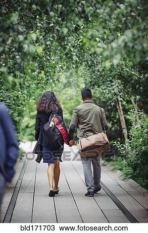 Stock Image - Couple walking on wooden walkway in park. Fotosearch