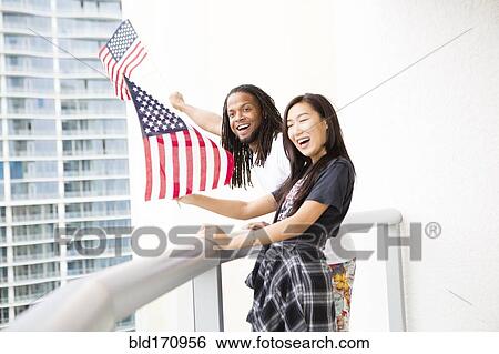 Couple waving American flags on urban balcony View Large Photo Image Stock Photograph - Couple waving American flags on urban balcony. Fotosearch