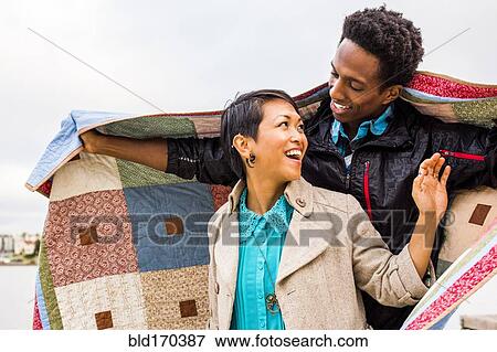 Stock Photo - Couple wrapping themselves in blanket outdoors. Fotosearch