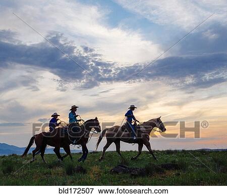 Stock Photo - Cowgirls and cowboy riding horses in rural field. Fotosearch