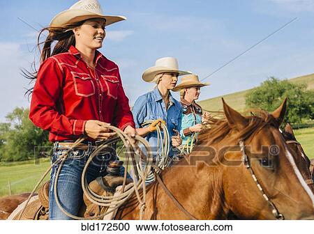 Stock Image - Cowgirls riding horses on ranch. Fotosearch