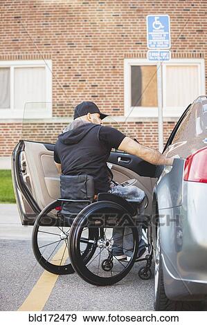 Stock Photo - Disabled man in wheelchair climbing into car. Fotosearch