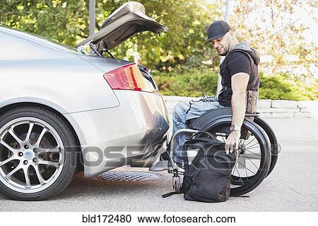 Stock Image - Disabled man in wheelchair packing car trunk. Fotosearch
