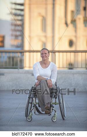 Stock Image - Disabled woman sitting in wheelchair on urban rooftop. Fotosearch
