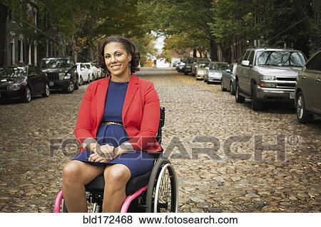 Stock Photo - Disabled woman smiling in wheelchair on cobblestone street. Fotosearch