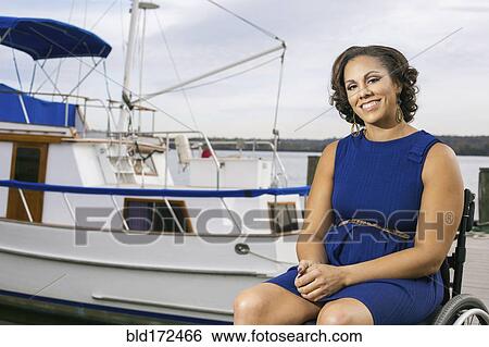 Stock Photograph - Disabled woman smiling in wheelchair on harbor. Fotosearch