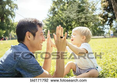 Stock Image - Father and son playing in grass in park. Fotosearch
