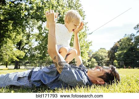 Stock Image - Father and son playing in grass in park. Fotosearch