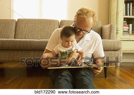 Stock Image - Father reading to son on living room floor. Fotosearch