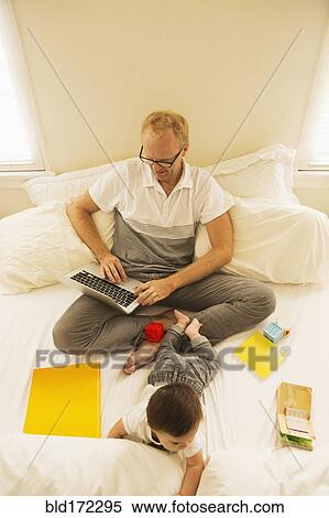 Father using laptop and playing with son on bed View Large Photo Image Stock Photography - Father using laptop and playing with son on bed. Fotosearch