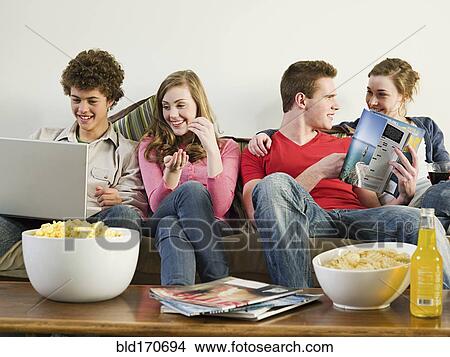 Picture - Friends relaxing on sofa in living room. Fotosearch