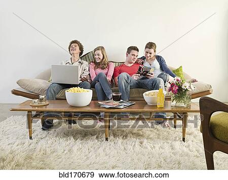 Friends relaxing on sofa in living room View Large Photo Image Stock Photo - Friends relaxing on sofa in living room. Fotosearch