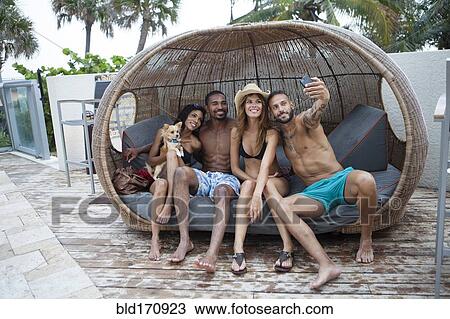 Stock Image - Friends taking selfie with cell phone in cabana. Fotosearch