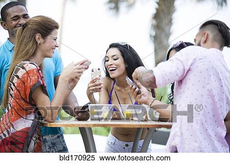 Friends using cell phone at table outdoors View Large Photo Image Stock Photography - Friends using cell phone at table outdoors. Fotosearch