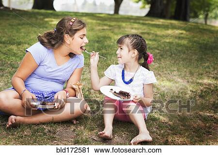 Stock Image - Girl feeding sister cake at birthday party in park. Fotosearch