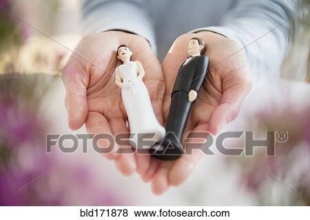 Stock Photo - Hands holding bride and groom cake toppers. Fotosearch