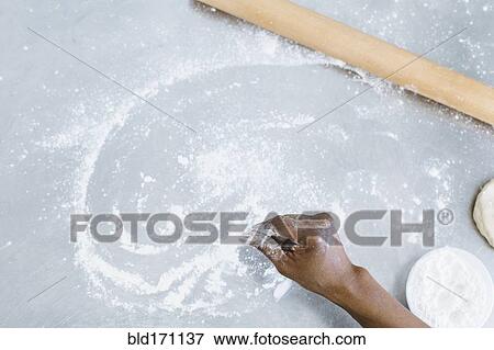 Stock Photo - High angle view of baker sprinkling flour on counter. Fotosearch
