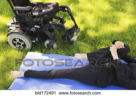 Stock Image - High angle view of disabled woman stretching legs in park. Fotosearch