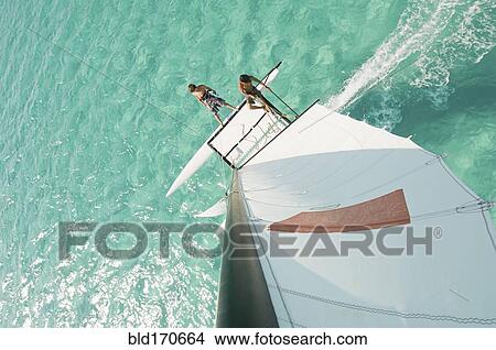 Picture - High angle view of men hoisting rigging on sailboat. Fotosearch