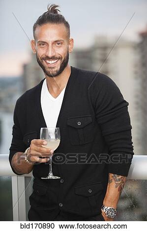 Stock Image - Hispanic man drinking wine on urban balcony. Fotosearch