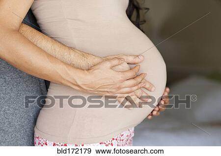 Stock Photo - Hispanic man hugging belly of pregnant wife. Fotosearch