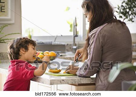 Stock Photograph - Hispanic mother and son eating fruit in kitchen. Fotosearch