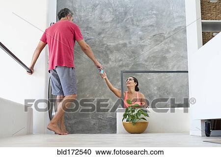Stock Image - Hispanic woman reaching for boyfriend in modern living room. Fotosearch