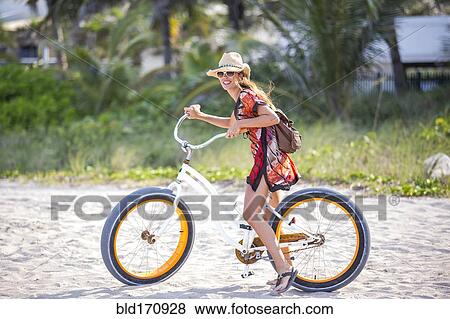 Stock Photo - Hispanic woman riding bicycle on beach. Fotosearch