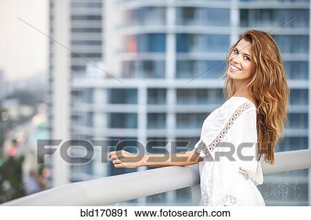 Stock Image - Hispanic woman standing on urban balcony. Fotosearch