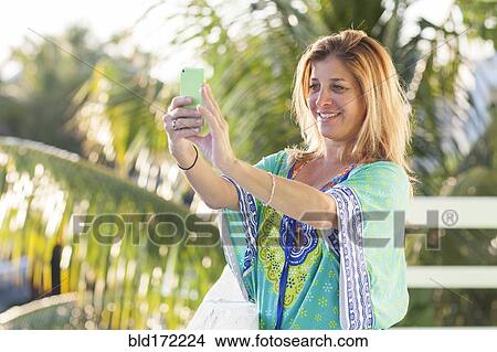 Picture - Hispanic woman taking selfie with cell phone on patio. Fotosearch