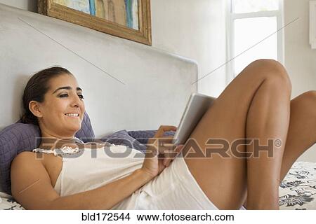 Picture - Hispanic woman using digital tablet on bed. Fotosearch
