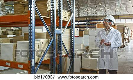 Stock Photo - Hispanic worker checking inventory in factory. Fotosearch