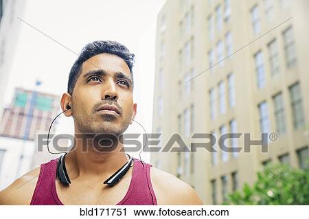 Stock Image - Indian athlete listening to earbuds in city. Fotosearch