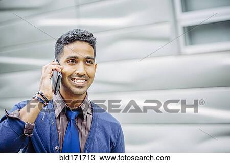 Stock Image - Indian businessman talking on cell phone outdoors. Fotosearch