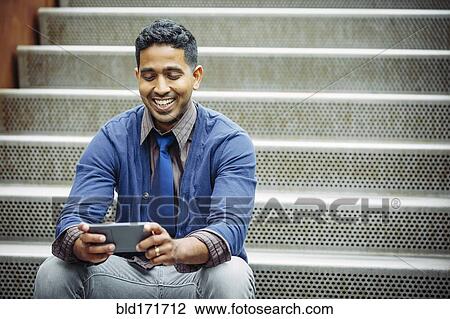 Stock Image - Indian businessman using cell phone on steps. Fotosearch