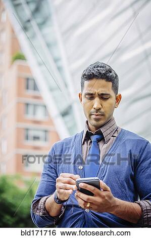 Stock Photograph - Indian businessman using cell phone outdoors. Fotosearch